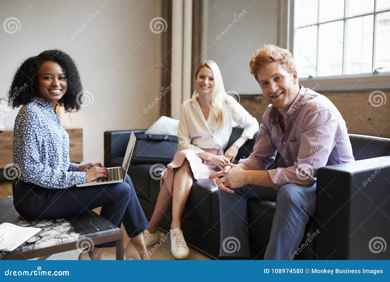 three young colleagues at a casual work meeting look to camera