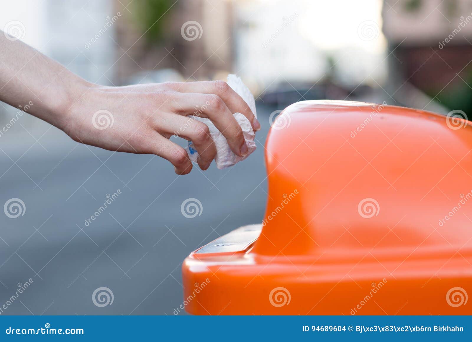 Throwing Waste into a an Orange Trash Can in the Street Stock Photo