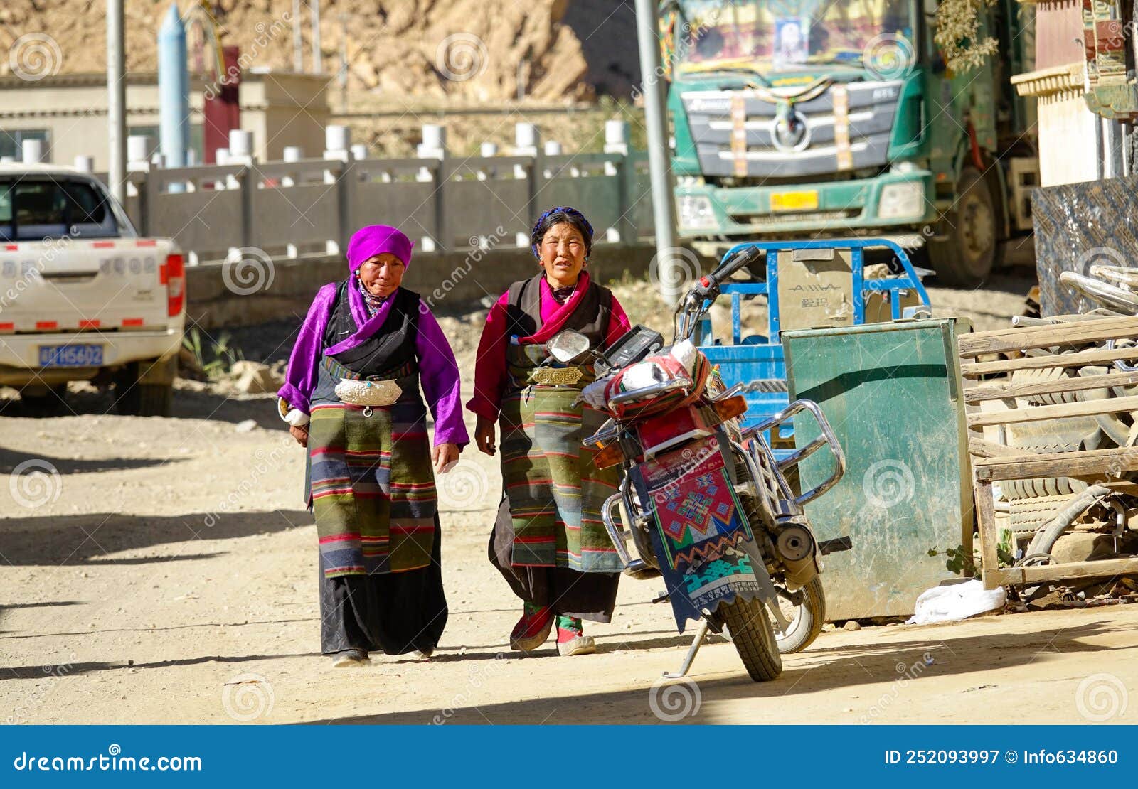 Two Senior Women In Colorful Traditional Clothes Walk Down The Unpaved