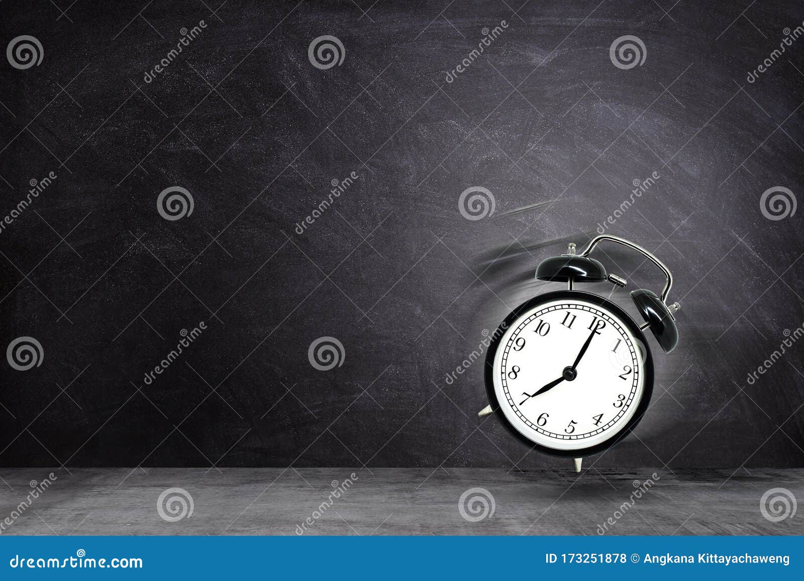 retro black alarm clock alerting at seven o`clock on chalkboard background.