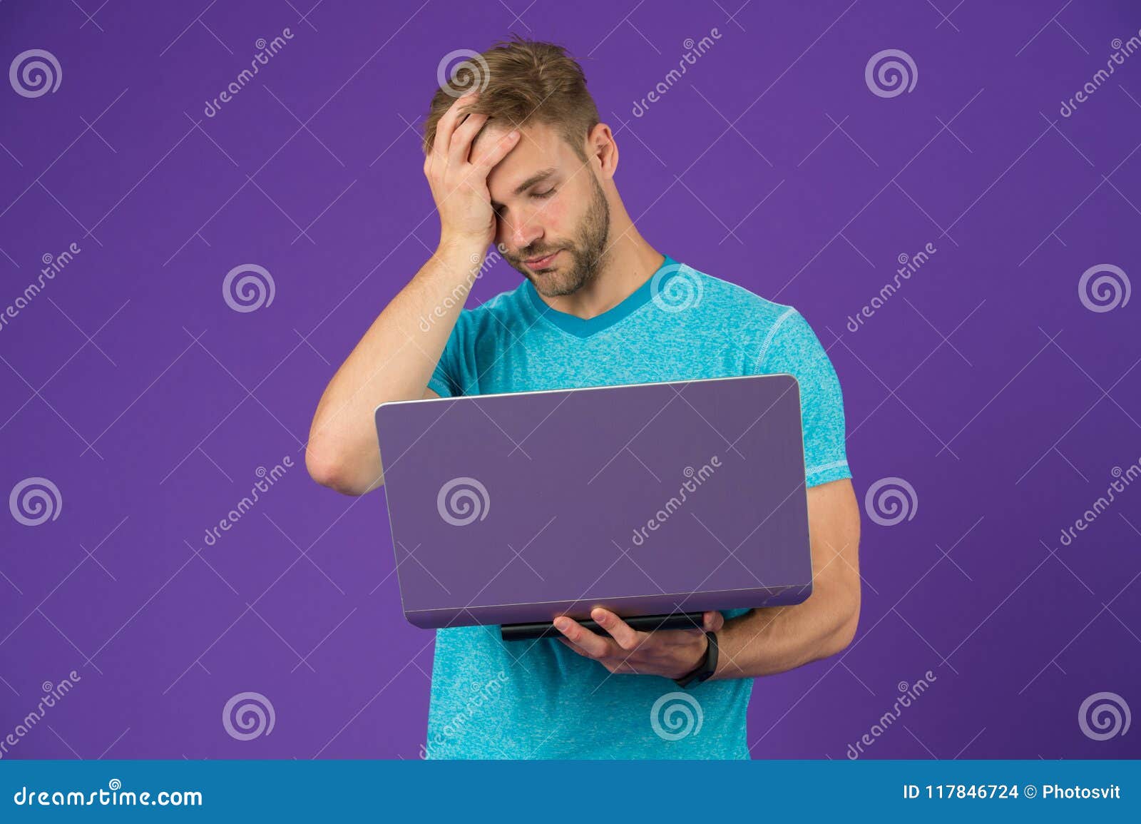 tired guy with computer on violet background. man in blue tshirt work on laptop on purple background. internet surfing