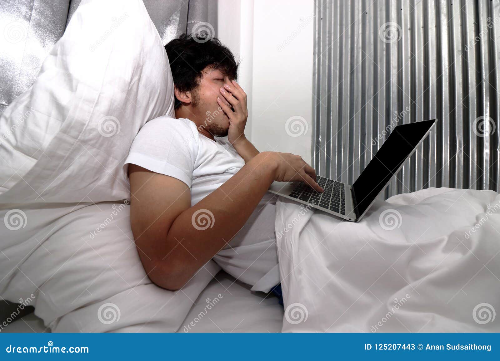 tired laziness asian man working on laptop on the bed in bedroom.