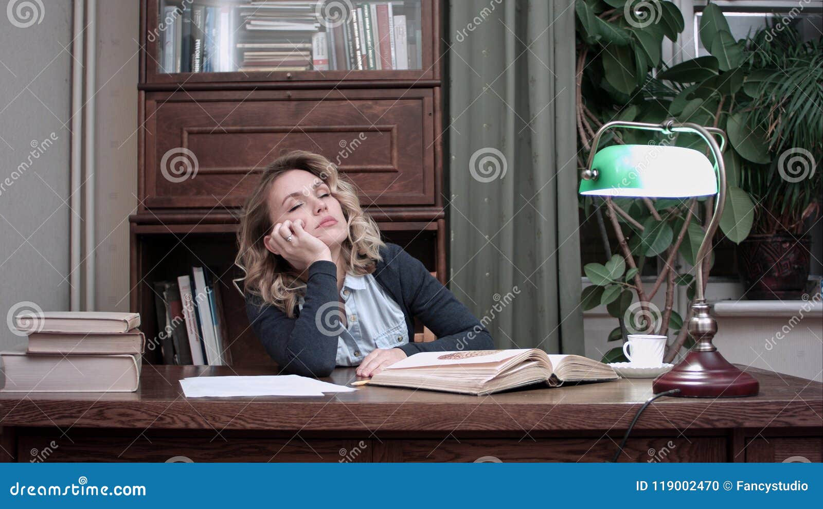 Tired Young Woman Falling Asleep Over A Book While Sitting At The