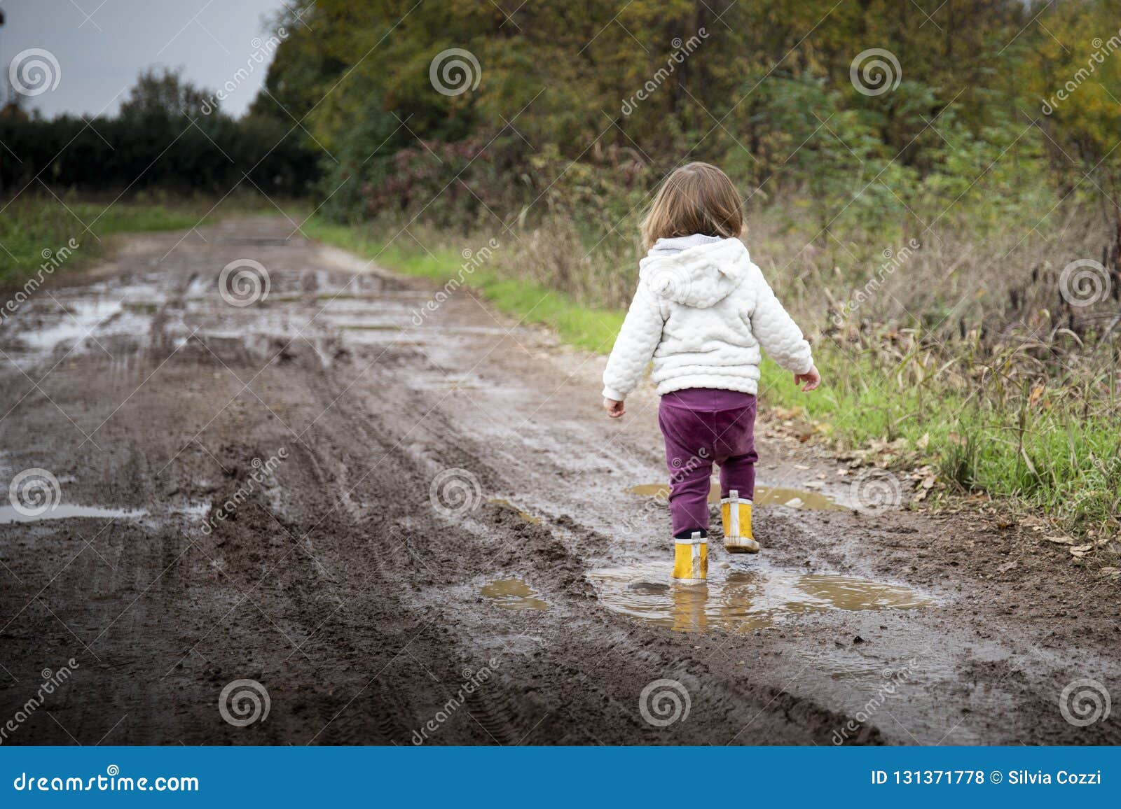 toddler splashing in puddles in muddy country road