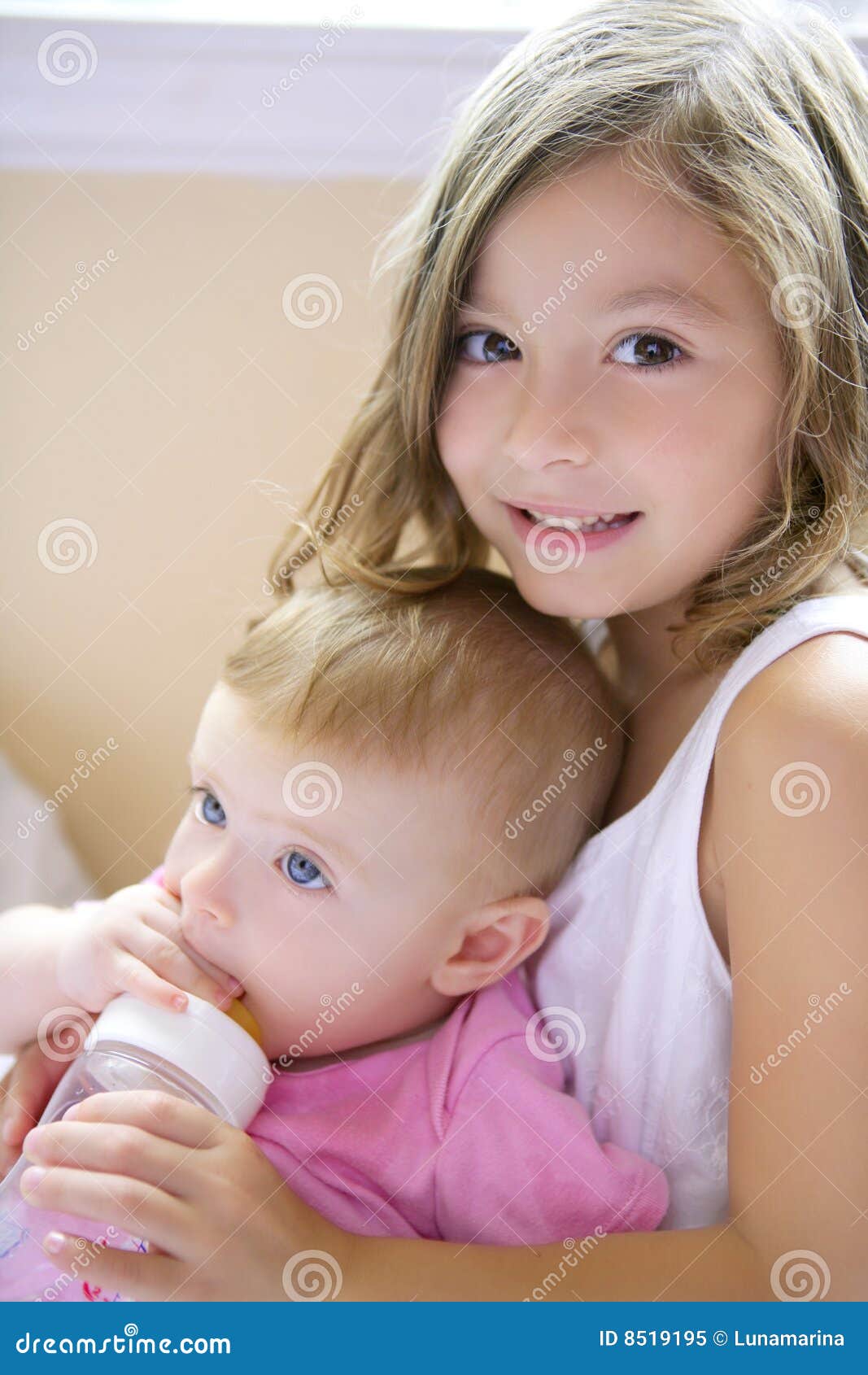 Toddler Girl Giving Bottle Of Milk To Baby Sister Stock I