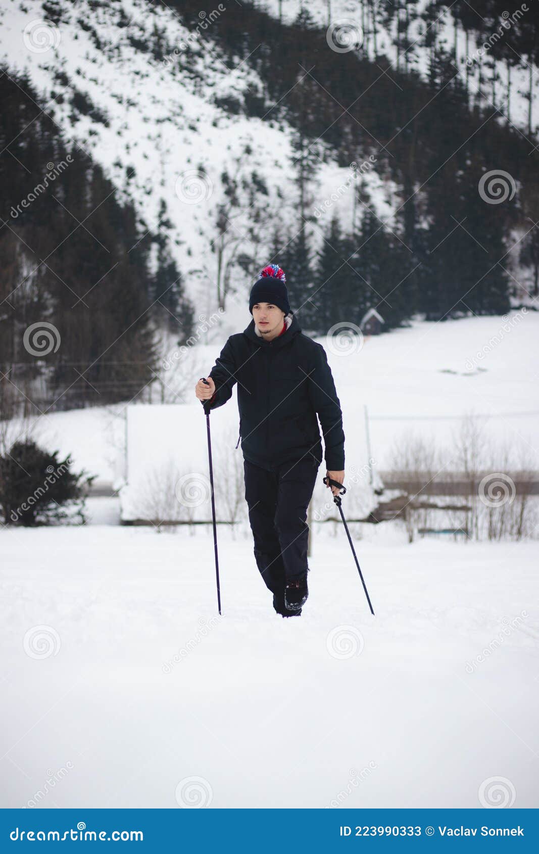 Toma De Un Hombre Con Ropa Deportiva De Invierno Y Un Sombrero Con Pompa  Mientras Sube a La Cima De Una Montaña Nevada Usando Post Imagen de archivo  - Imagen de checo