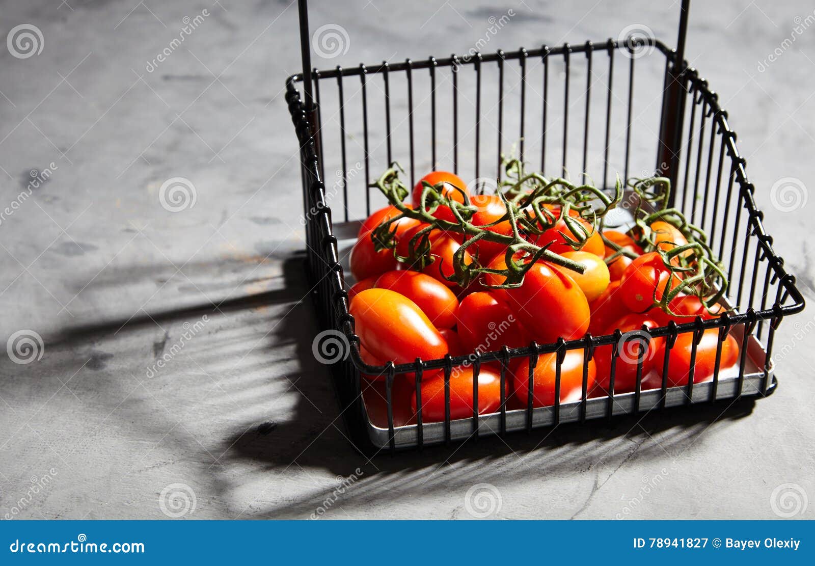 Tomates de cereza frescos en rama en cesta del hierro. Tomates de cereza frescos, jugosos, maduros en rama en cesta del hierro en fondo gris Tomates de cereza para adornar el plato acabado, salmuera o a secarse Luz direccional, foco selectivo, espacio para el texto