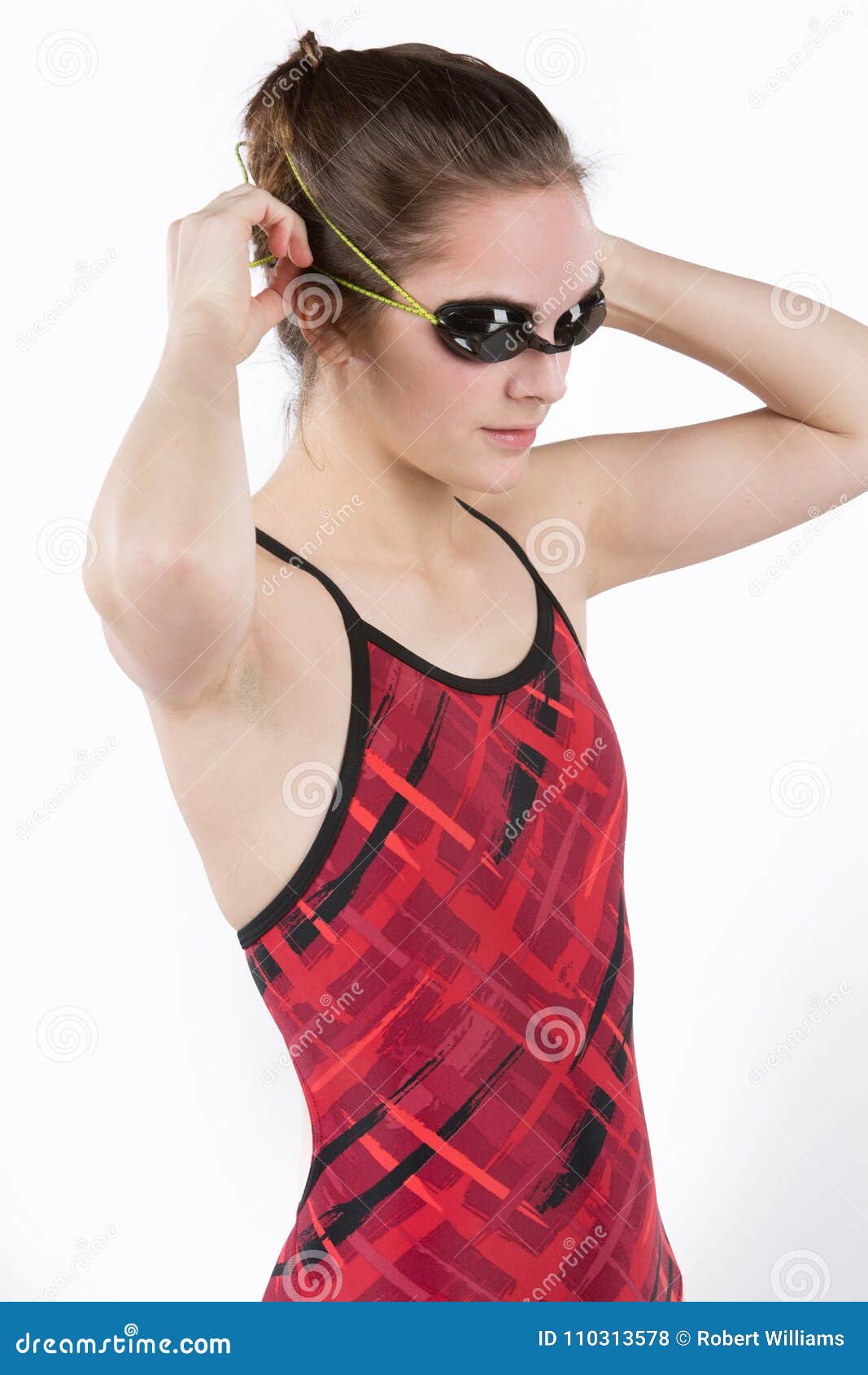 Tonårig flicka i konkurrensbaddräkt och skyddsglasögon. Den nätta tonåriga flickan som bär den röda baddräkten, med bad, rullar med ögonen Isolerat på vanlig bakgrund