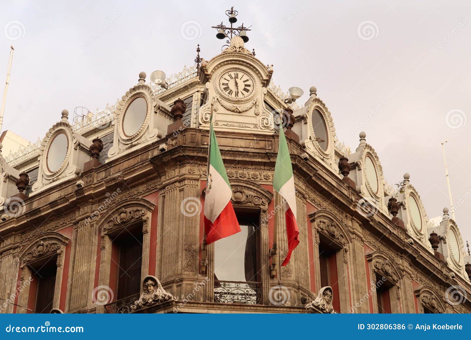 the top of building edificio la esmeralda with mexican flags, a clock, and many details and ornaments, mexico city