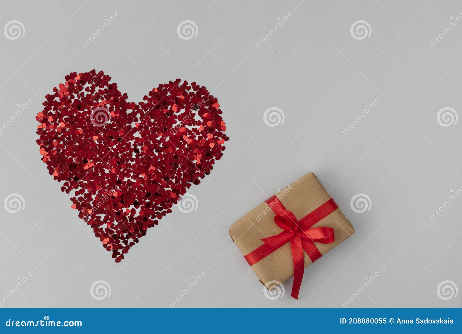 top view of big red heart made from little glittering confeti of heart s, gift box with red ribbon is near,