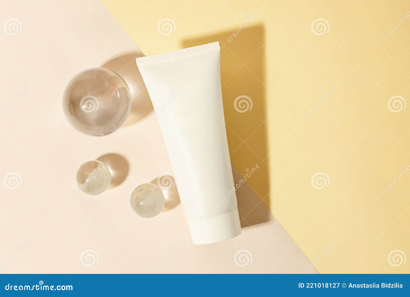 top view of the blank cosmetics tube on the dual pastel background.glass sphers near it,concept of the cleanness and clarity.