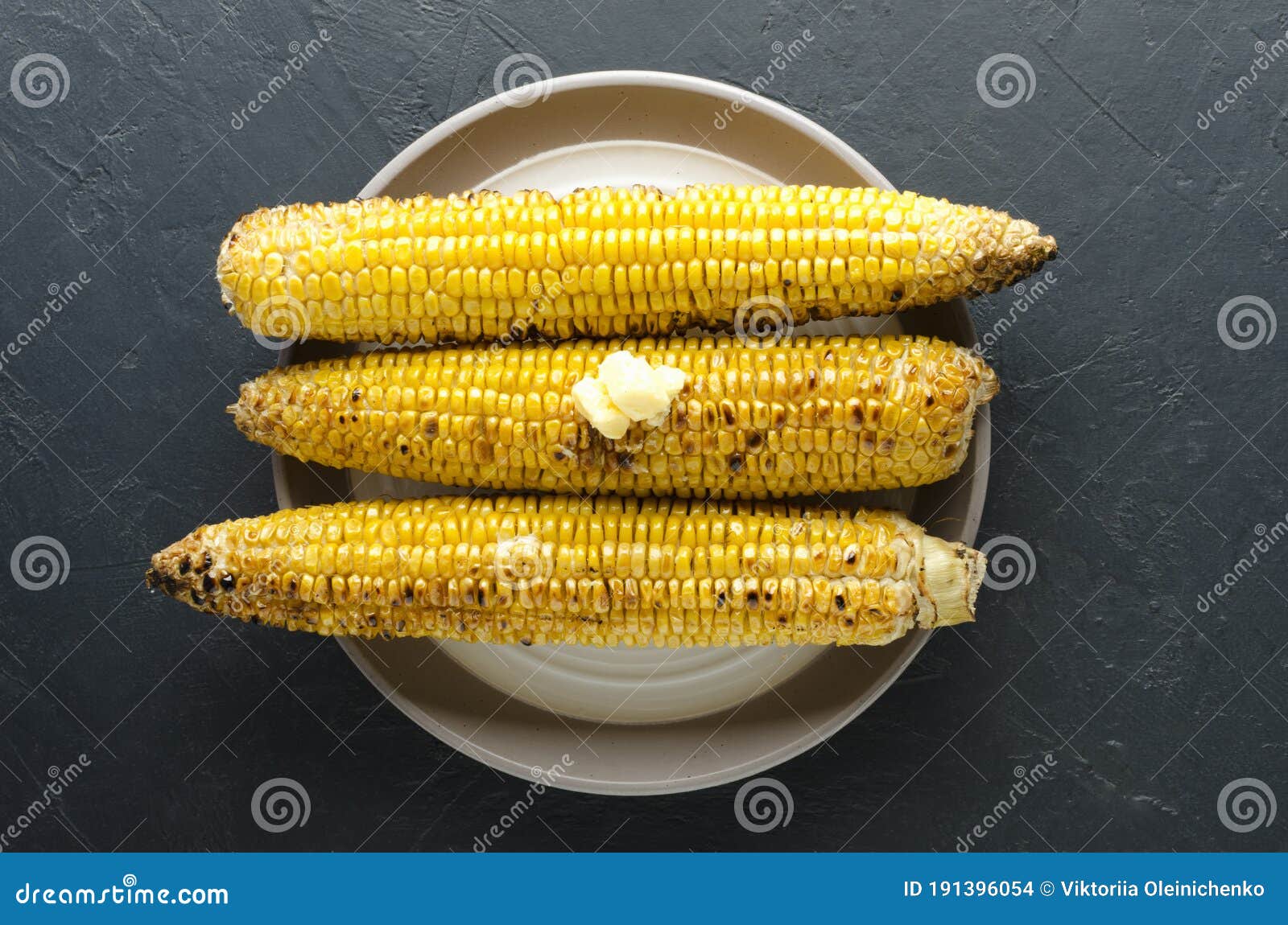 top view of cooked delicious corn with butter on the plate, dark table