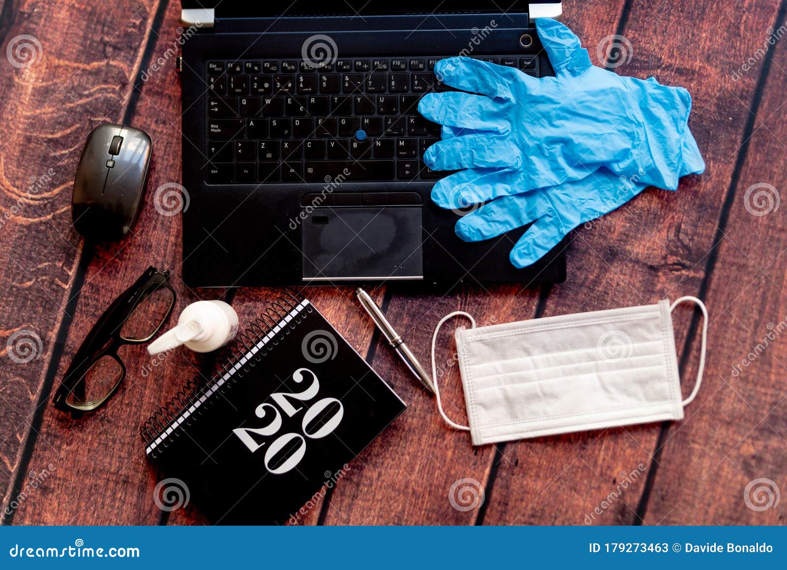 top view of coronavirus remote work kit on wooden office desk with hand sanitizer and face mask, a solution against the spread of