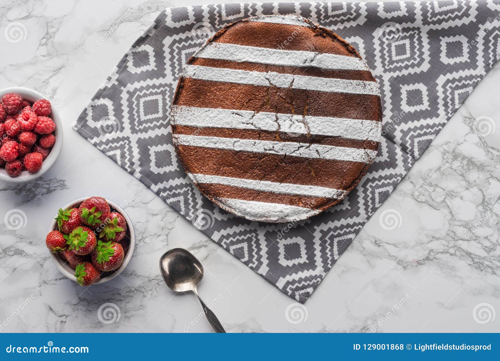 top view of delicious brown cake with sugar powder and fresh berries