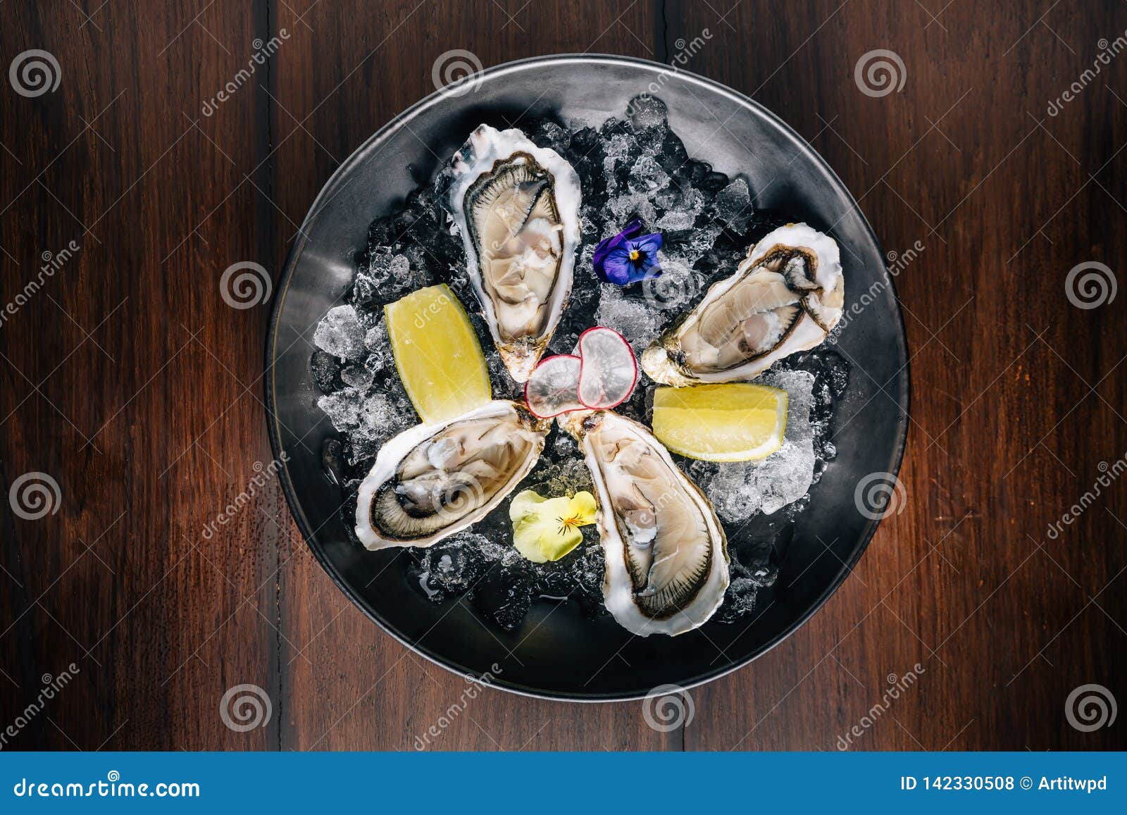 top view of fine de claire oyster and lemon served in black bowl with ice on wooden table