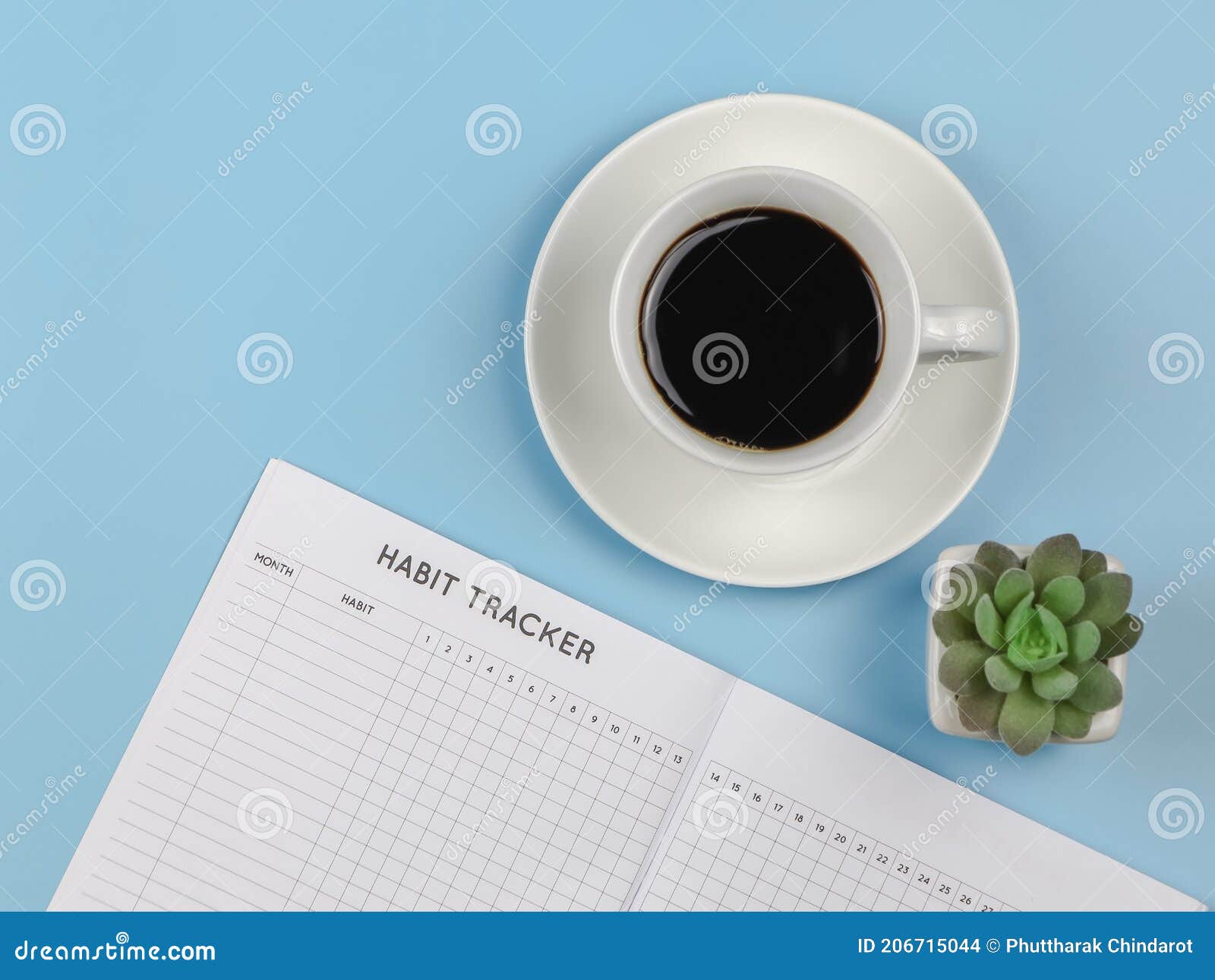 flat lay of habit tracker book with pen,  cup of black coffee and succulent plant pot on blue background with copy space
