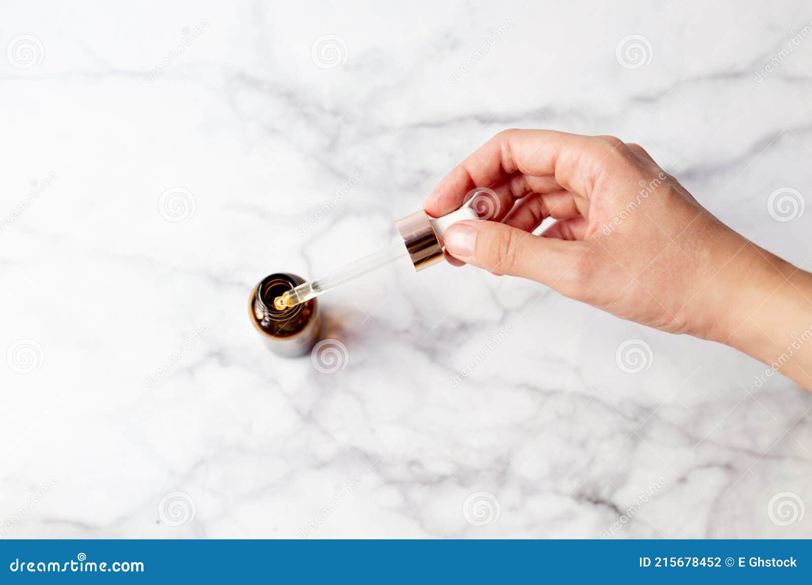 top view of hand holding a retinol oil serum pipette and oil bottle on  marble background. beauty care concept