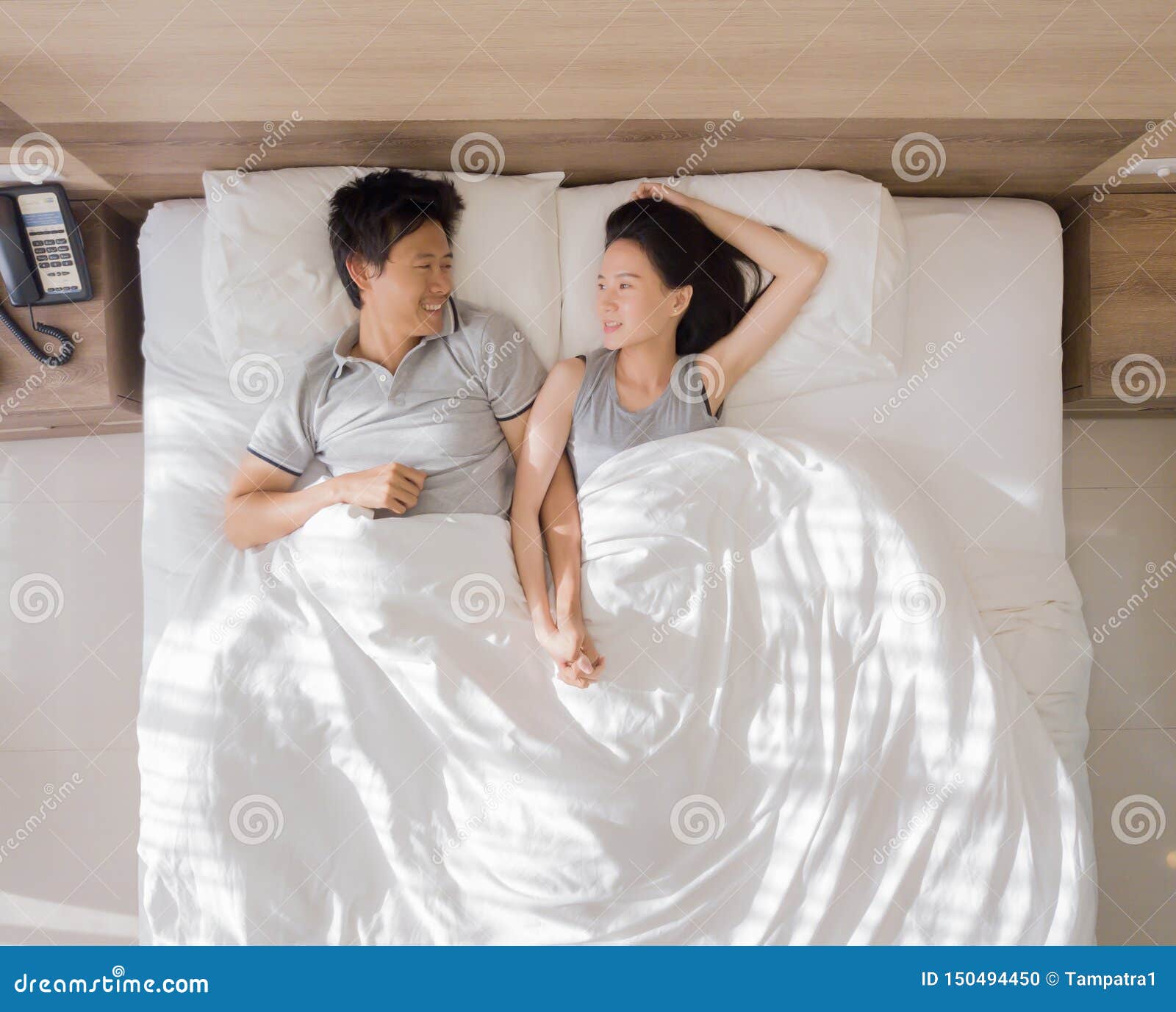 Top View of Happy Asian Couple Smiling, and Sleeping Together on Bed in Love and Sex Concept in a Modern Bedroom with White Stock Photo