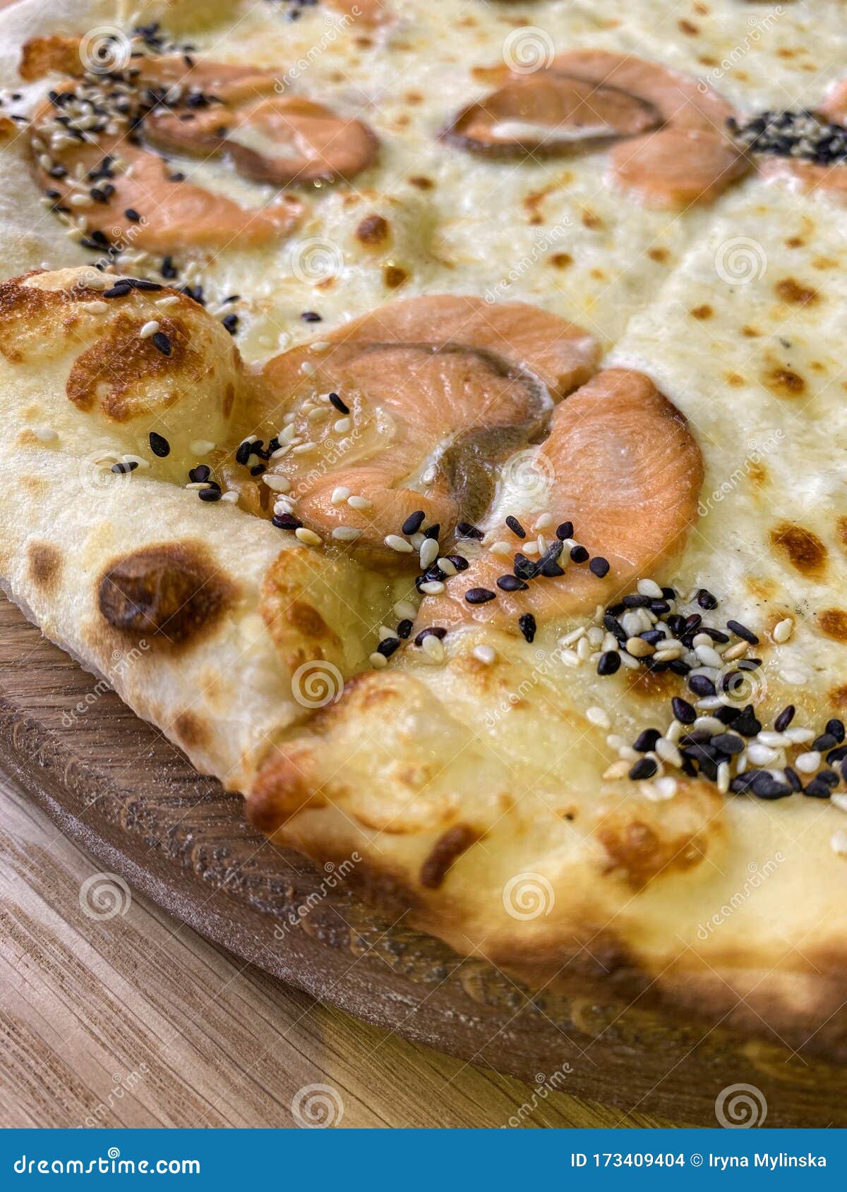 top view on hot seafood pizza on wooden plate. fried yeasted flatbread topped with red fish, salmon or trout fillets and black and