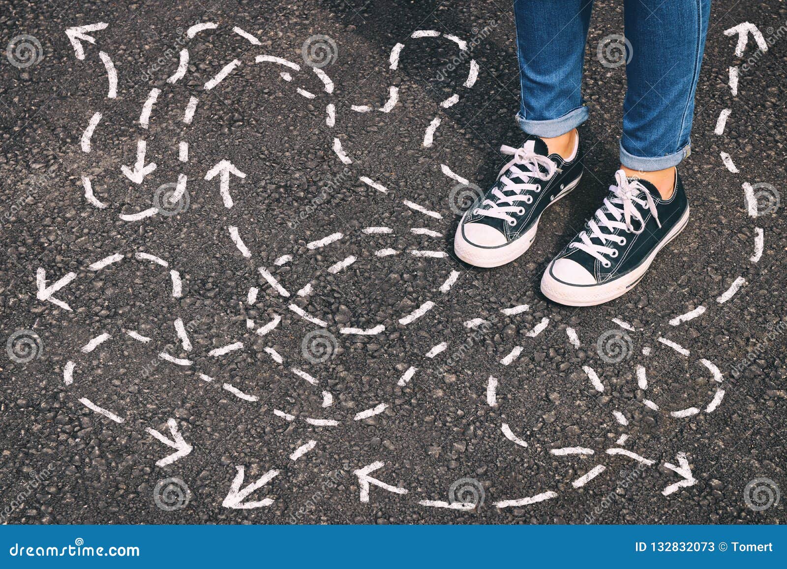 top view image of person in jeans and retro shoes standing over asphalt road with painted arrows showing different directions.