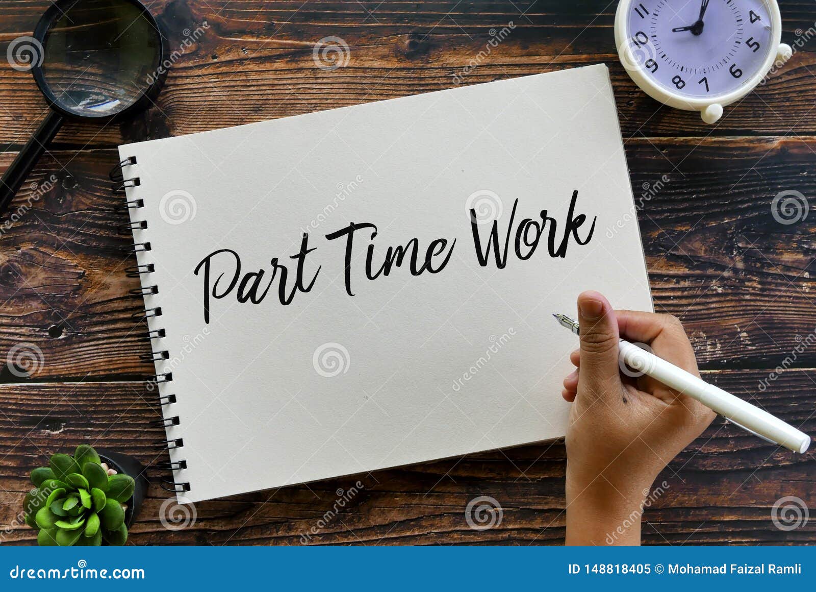 top view of magnifying glass,plant,clock and hand holding pen writing part time work on notebook on wooden background