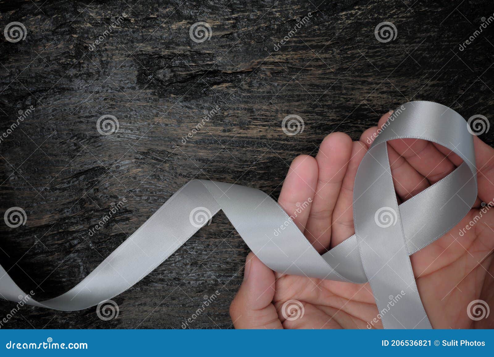 top view of male hands holding gray ribbon on dark wood background with copy space. brain cancer tumor awareness concept.