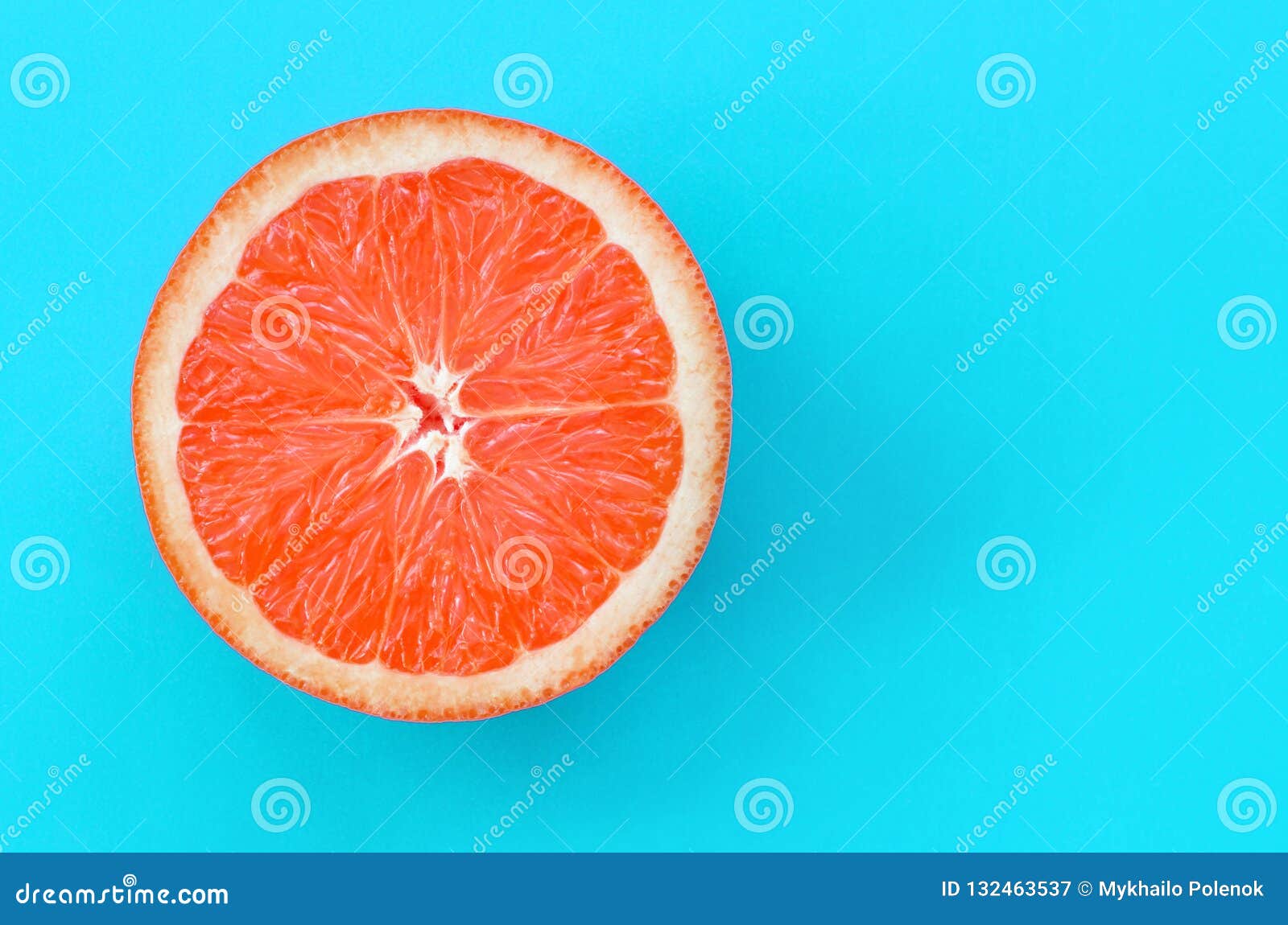 top view of an one grapefruit slice on bright background in blue color. a saturated citrus texture image