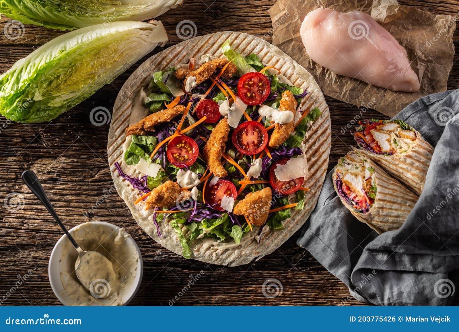 top view of open tortilla with chicken nuggets, chery tomatoes, red cabbage, salad, carrot stripes and parmesan shavings