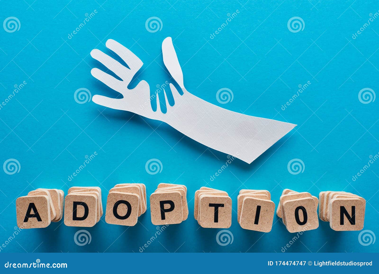 top view of paper cut parent and child hands and adoption lettering on blue background.