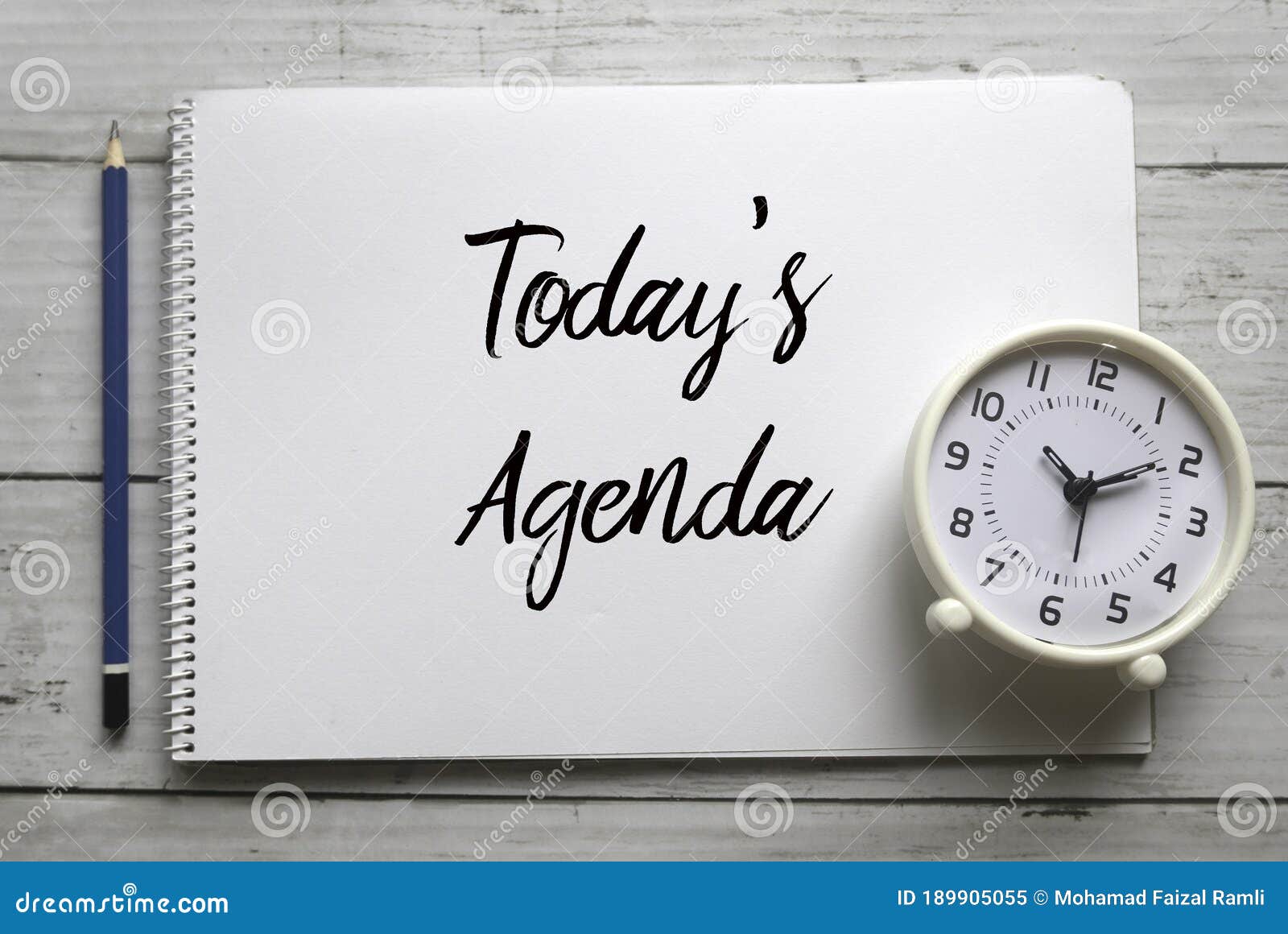 top view of pencil,clock and notebook written with today`s agenda on white wooden background