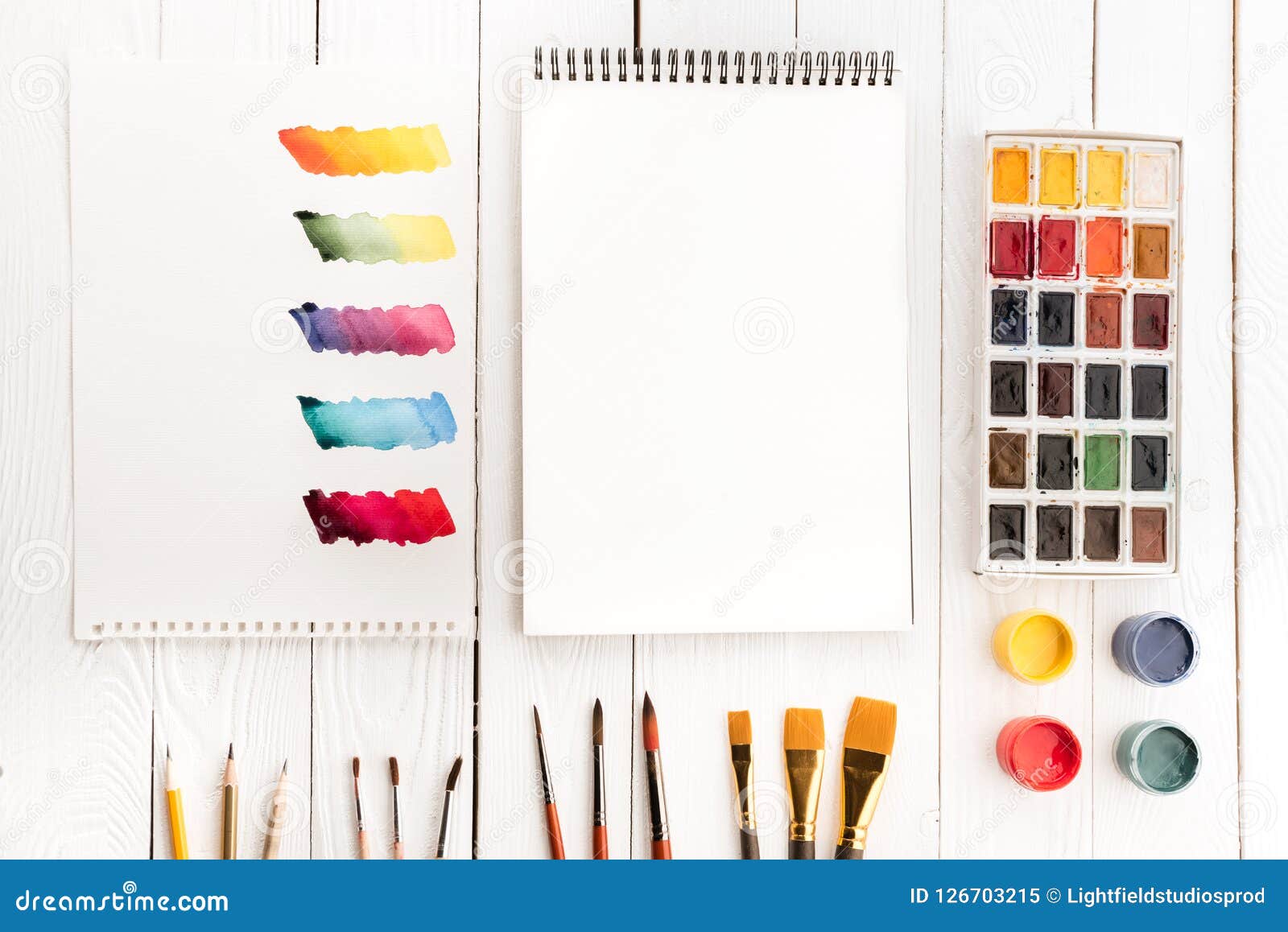 top view of set of paints different brushes blank notebook and colorful brushstrokes