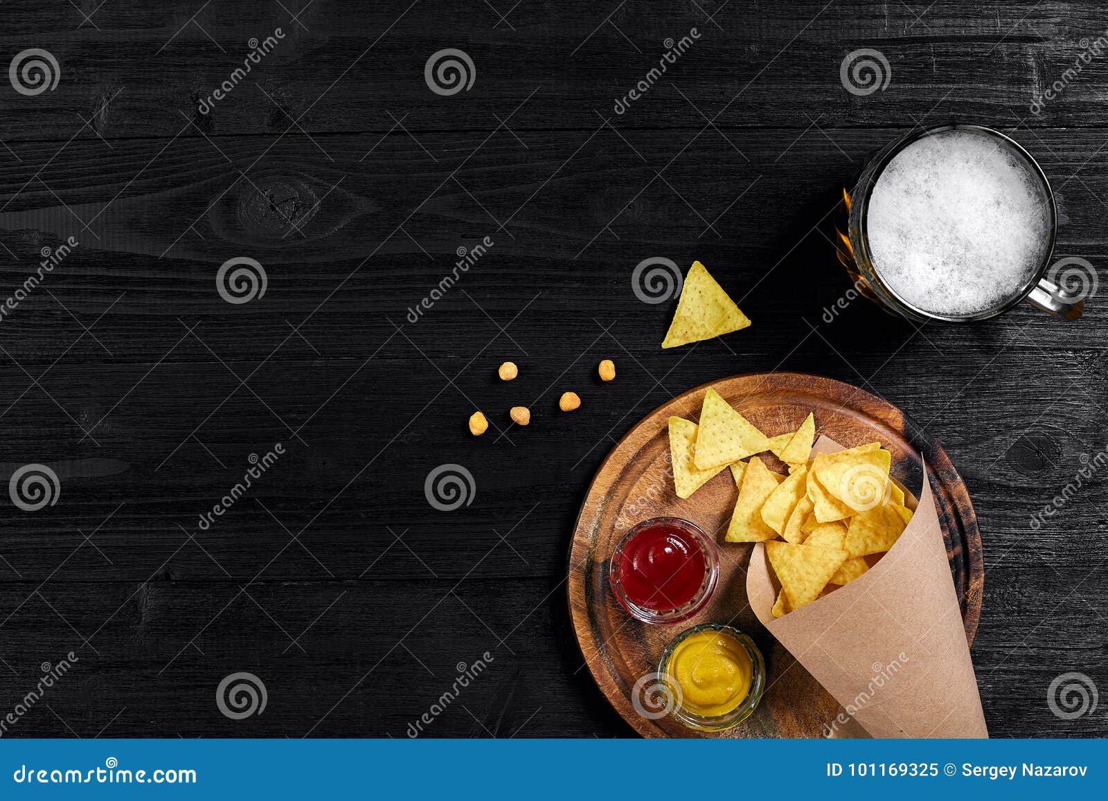top view of tortilla chips with sauce, glass of beer on black wooden background