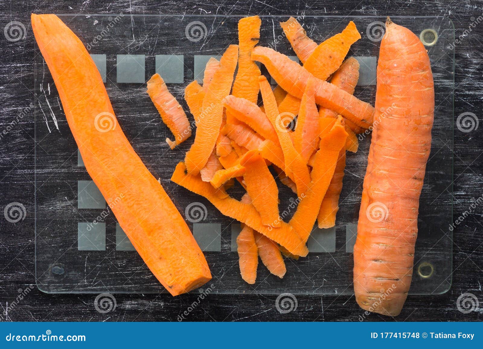 top view of unpeeled carrot and peeled carrot with peeling on glass cutting board on the black background
