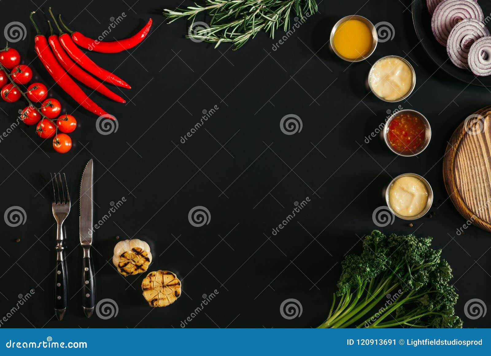 top view of various sauces, grilled garlic, fork with knife and fresh vegetables with herbs