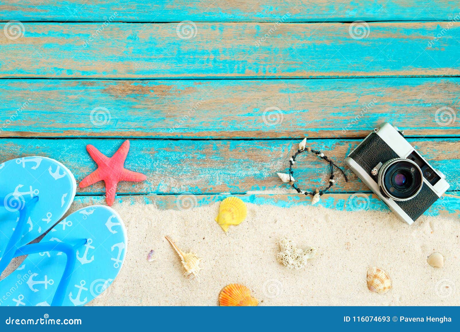 top viwe of beach sand with slipper, starfish,shells, coral, retro camara and bracelet made of seashells on blue wooden backgroun