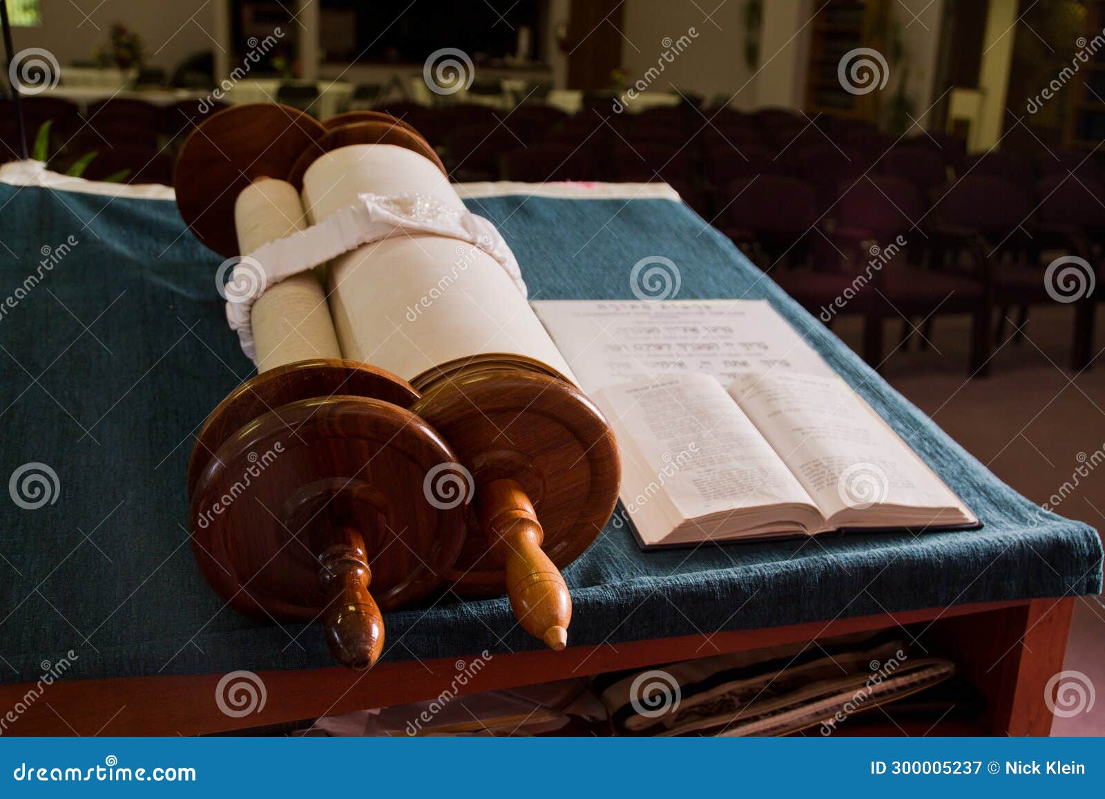 Torah Scroll on Blue Cloth with Empty Synagogue Chairs in Background
