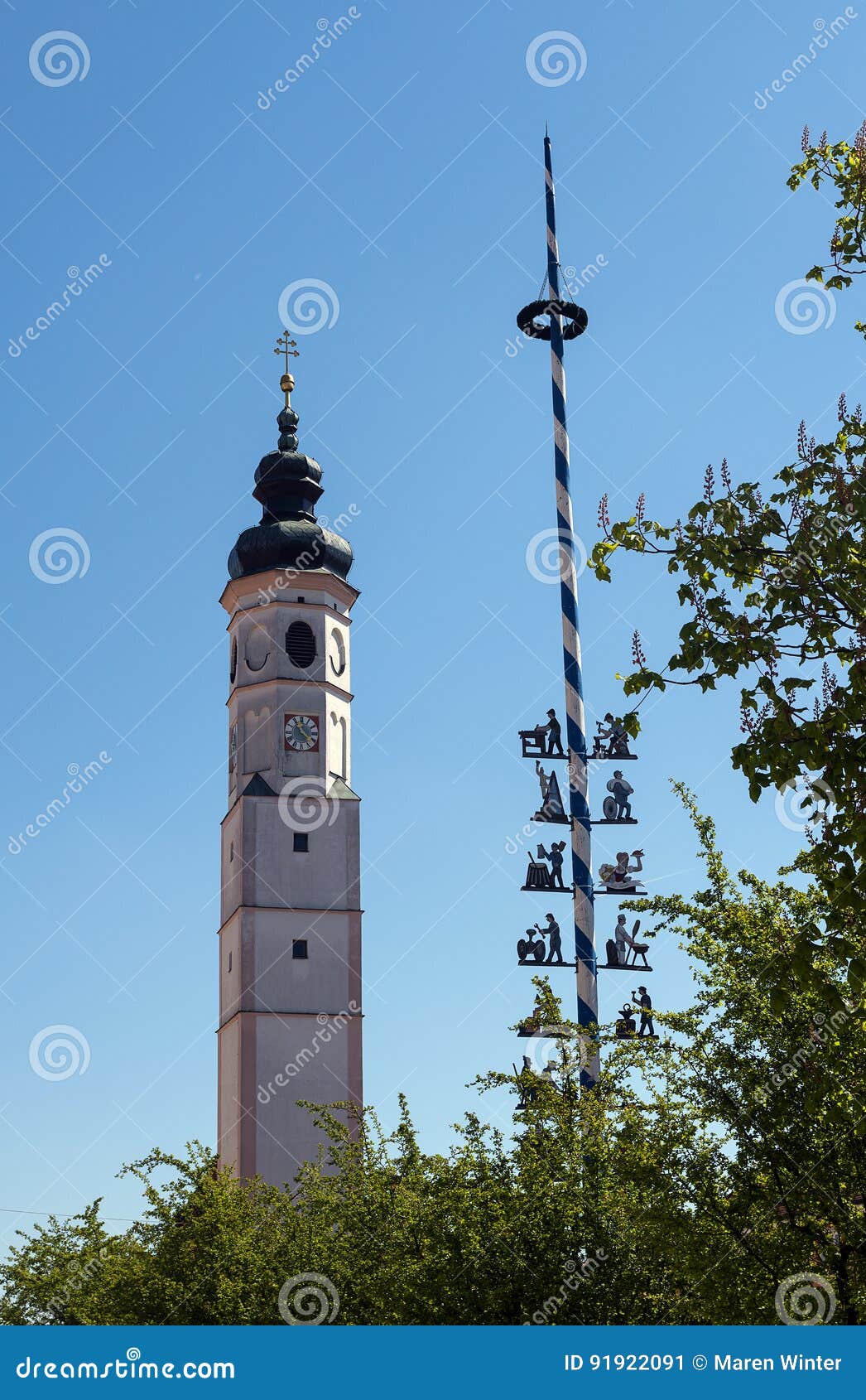 Torre de igreja bávara típica e um maibaum tradicional, maypole contra o céu azul em Dorfen, Baviera, Alemanha