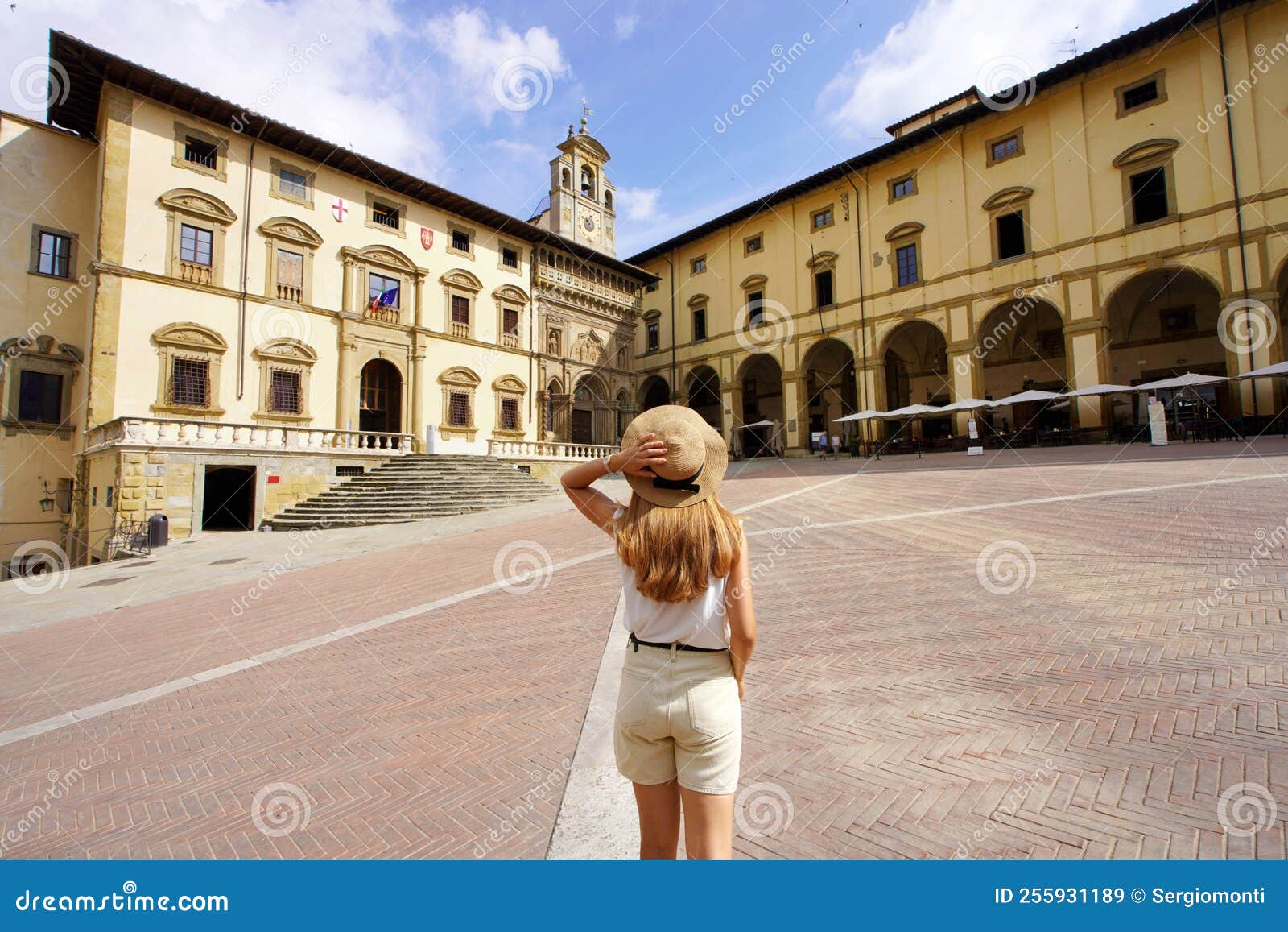 tourism in tuscany. back view of young traveler woman holding hat in piazza grande square in the old town of arezzo, tuscany,