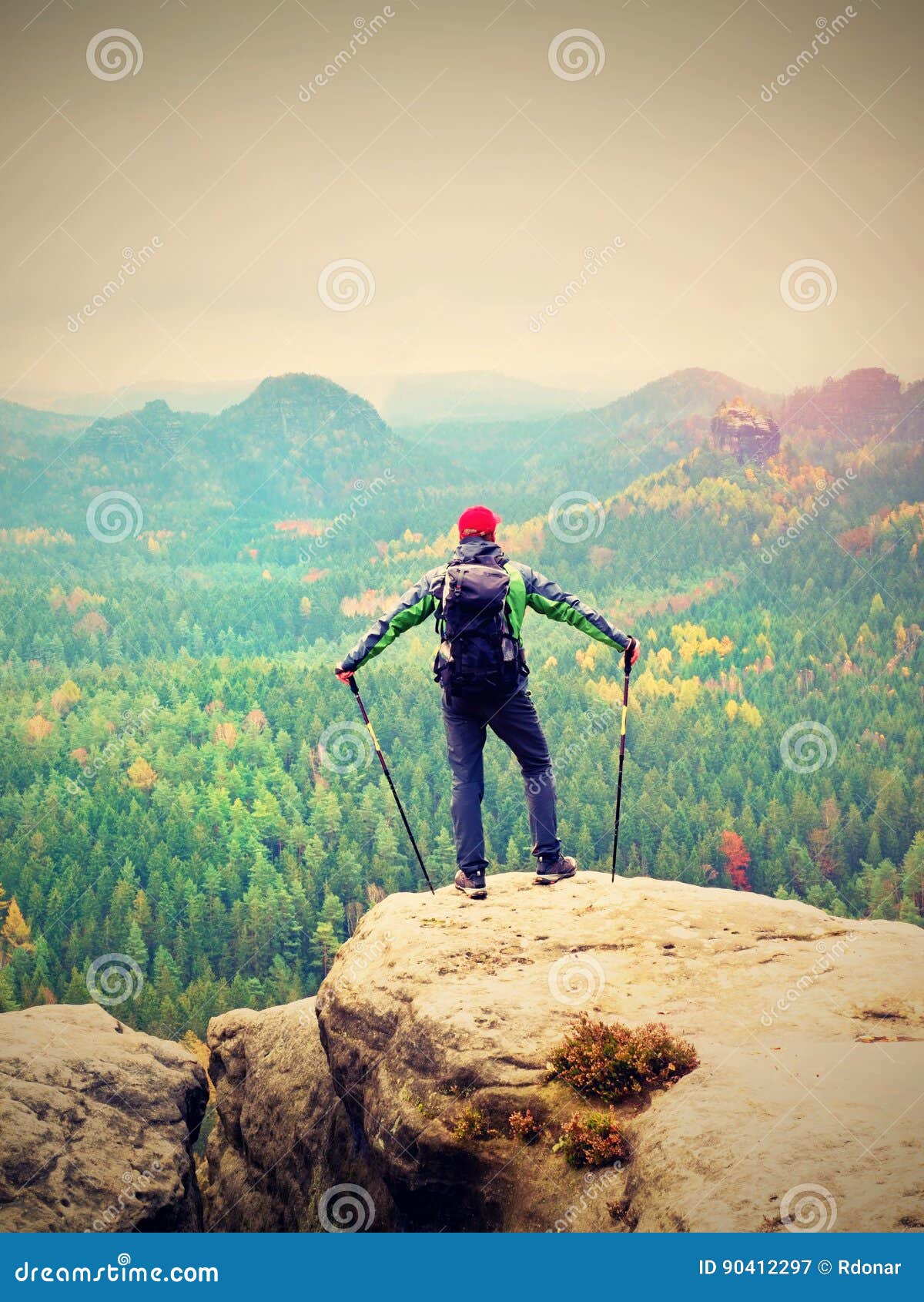 tourist guide on the summit with poles in hand and heavy backpack. hiker green jakcet nad red cap