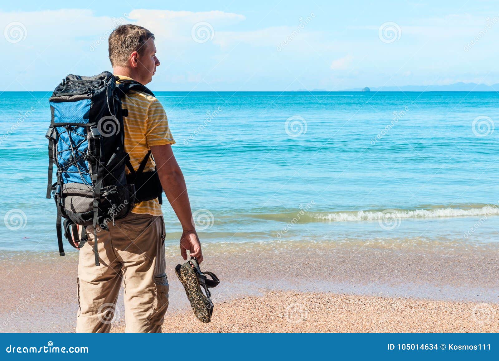 Tourist mit einem Rucksack verbringt Ferien auf dem Strand, bewundert eine schöne Ansicht