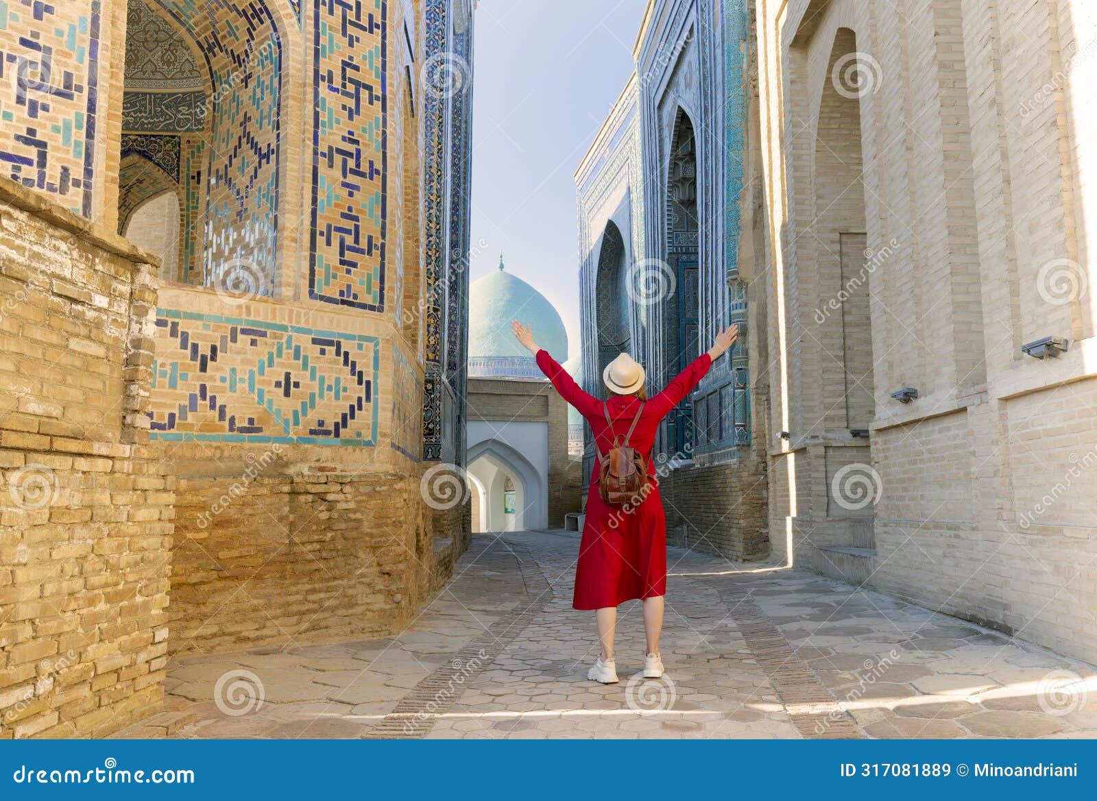 tourist woman in red dress clothes stands in the shah-i-zinda ensemble in samarkand, uzbekistan