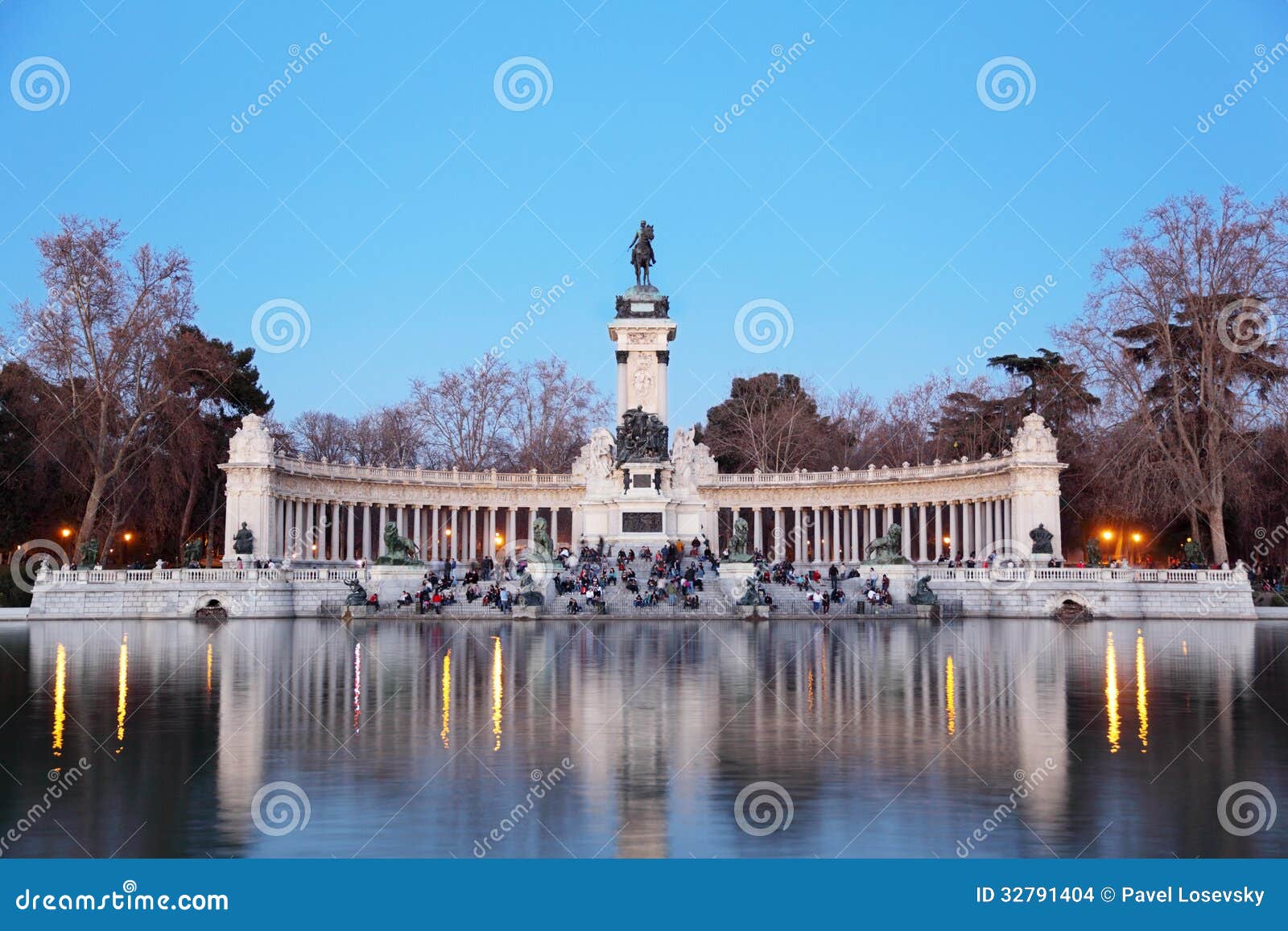 tourists sit near monument to alfonso xii at pond in retiro park