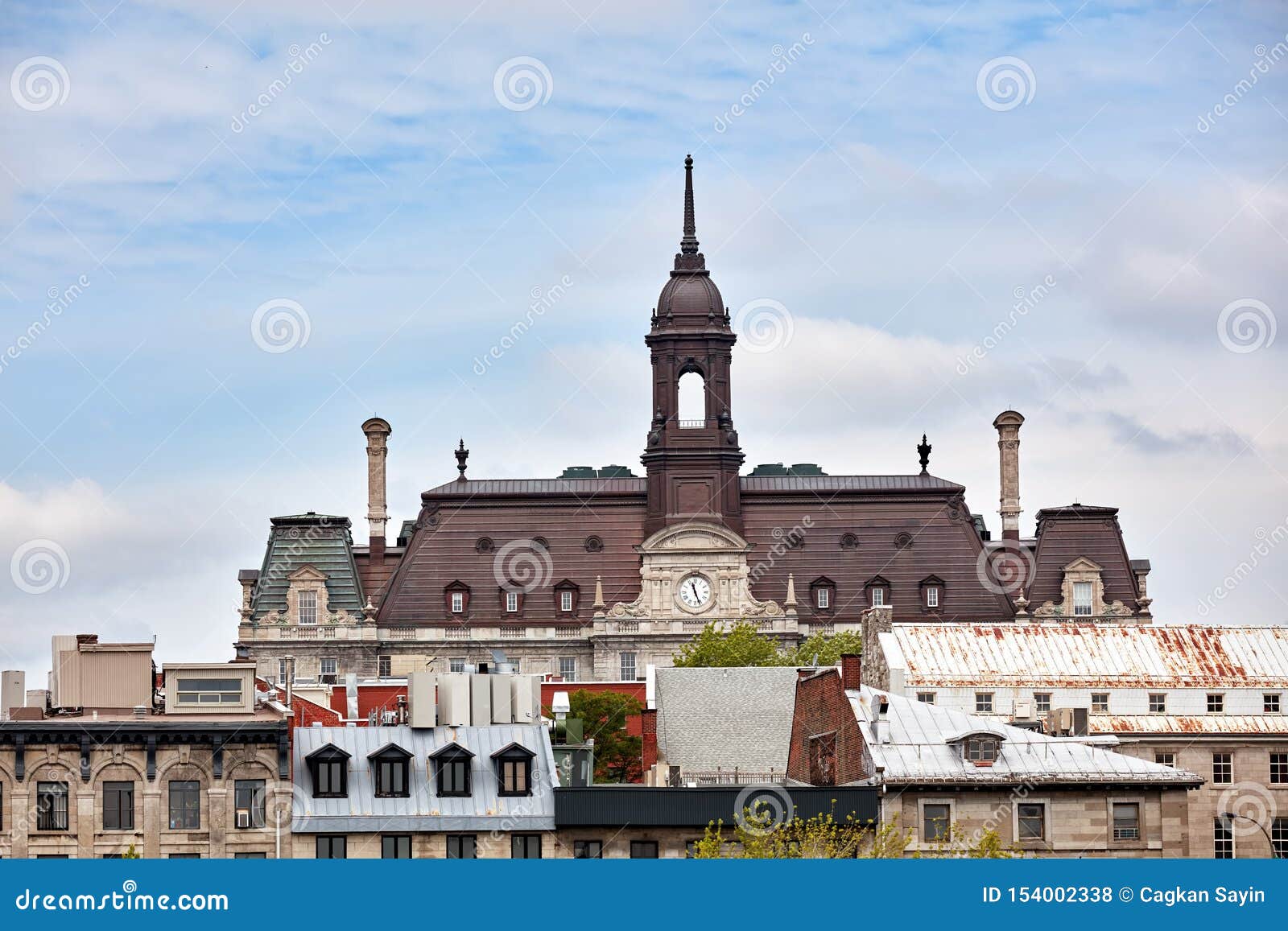 the tower, clock and roof of montreal city hall hotel de ville against bright cloudy sky in old montreal, quebec, canada