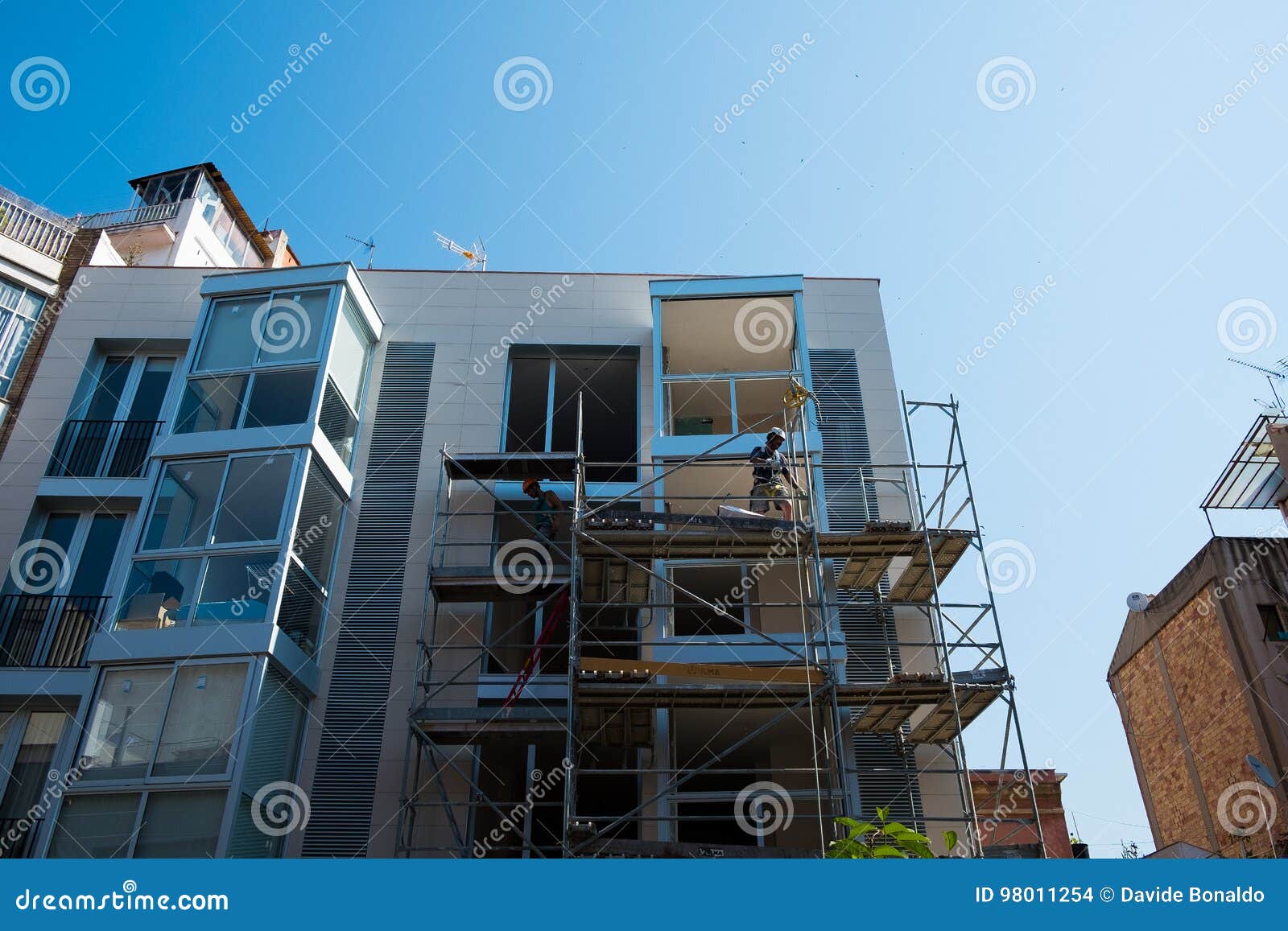 Trabajadores de construcción jovenes en el edificio del andamio en día soleado con el cielo azul claro. Trabajadores de Contruction en el edificio en día soleado