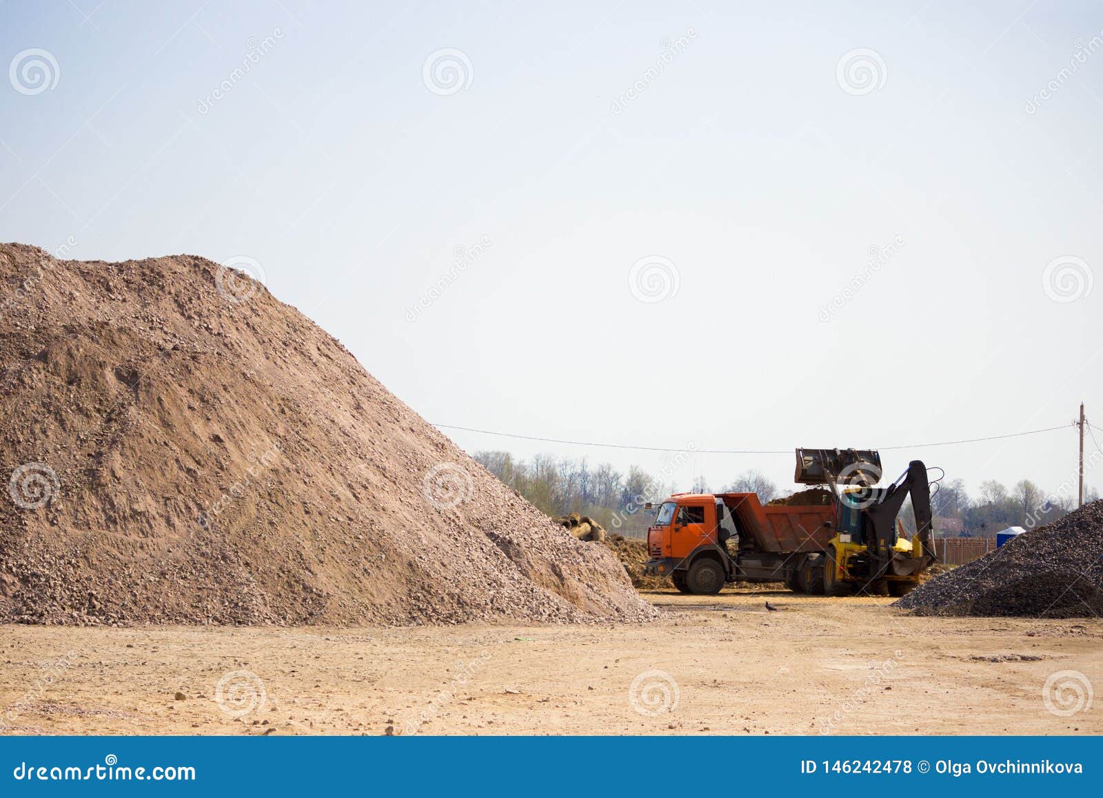 A Tractor is Loading Sand into a Truck Bed at a Construction Site. in