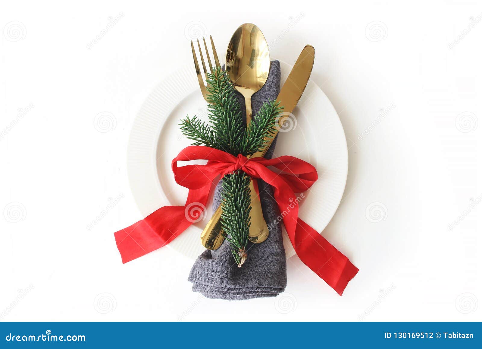 traditional christmas table place setting. golden cutlery, linen napkin, green spruce branches, plate and red ribbon