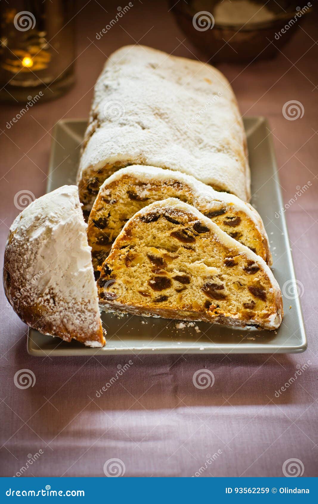 Traditional German Christmas stollen with raisins, nuts, candied fruits, sliced, powdered on plate, festive table setting, lit candle, closeup