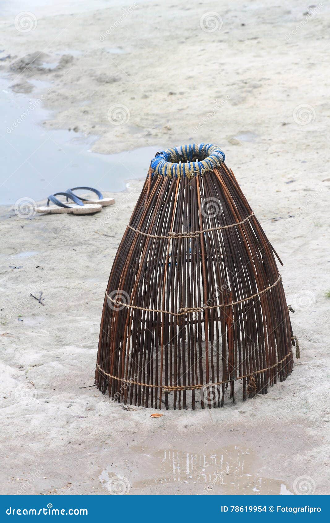 Traditional Handmade Fishing Trap and Flip Flops on Sand Stock
