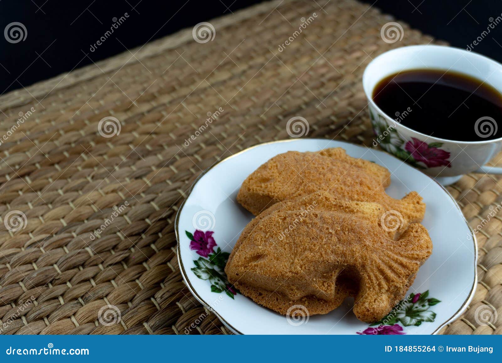 traditional malaysian cake called `kuih bahulu or baulu` in fish , in flowery plate with coffee over bamboo mat background