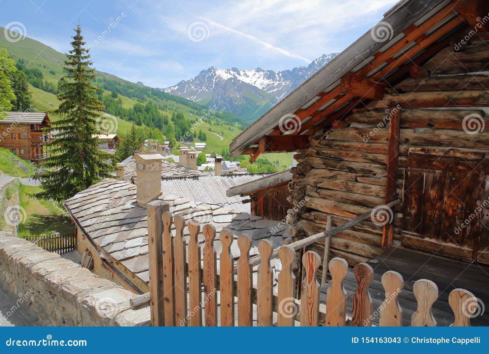 traditional roofs and a wooden house in saint veran village, with mountain range covered with snow and pine tree forests